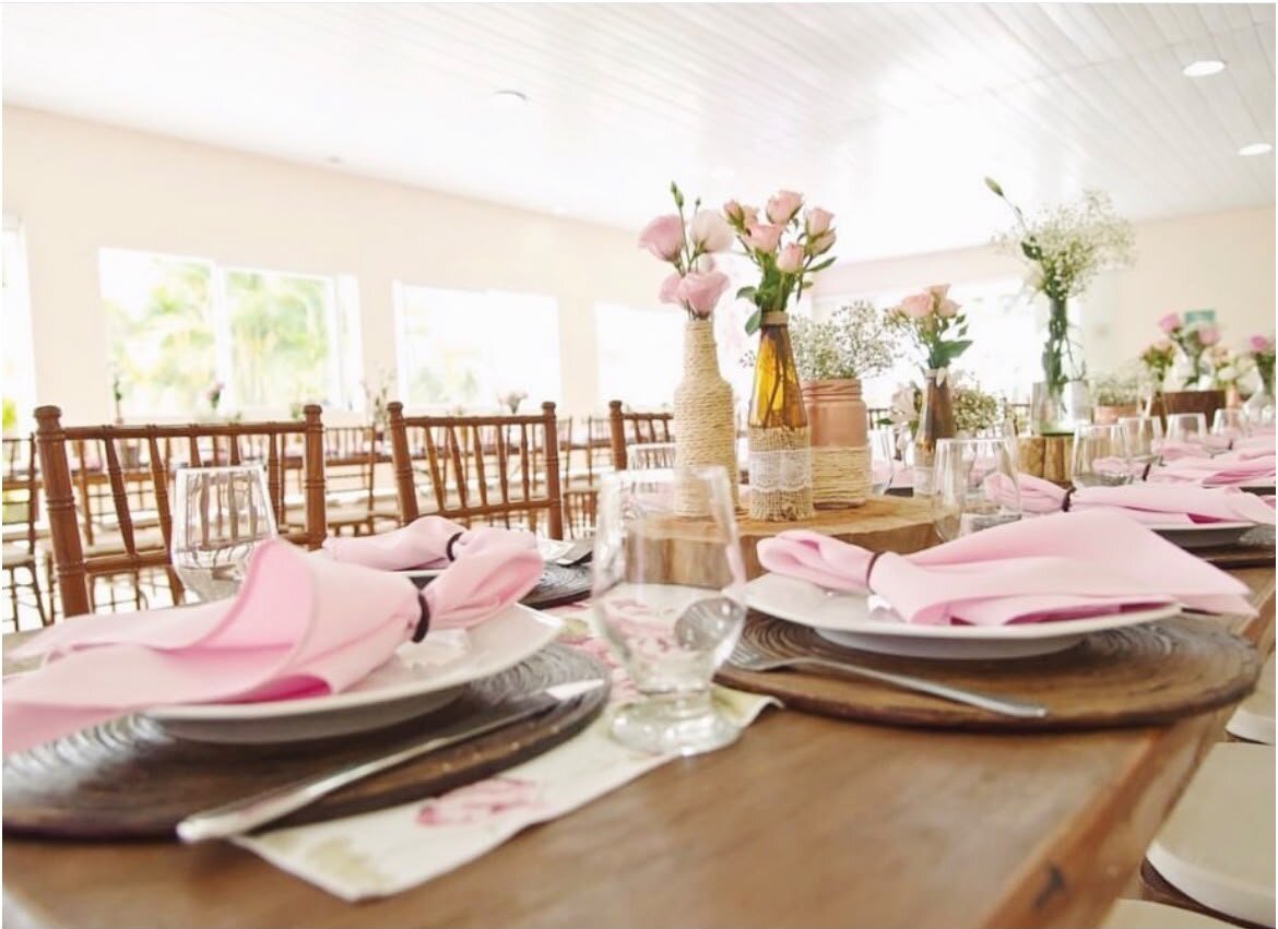 Mesa posta da Casa 1 com arranjos de flores, guardanapos rosa e taças.