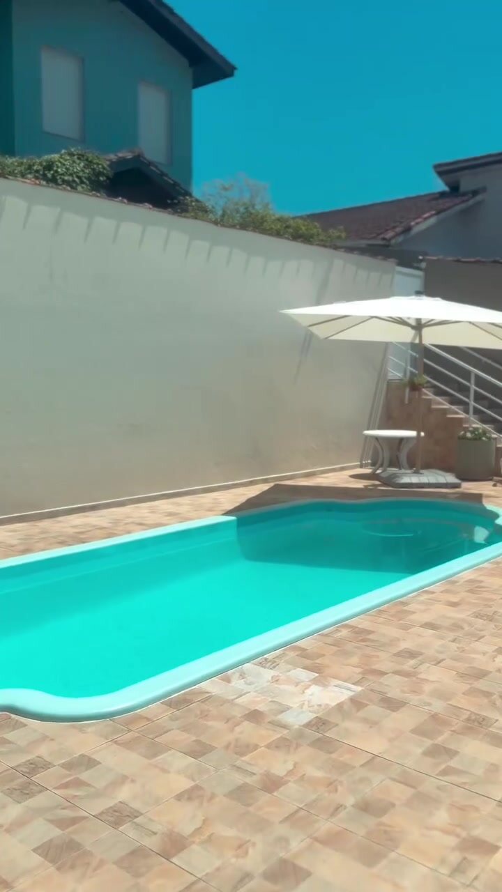 Piscina da Casa 1 em dia de céu azul, com guarda-sol aberto.