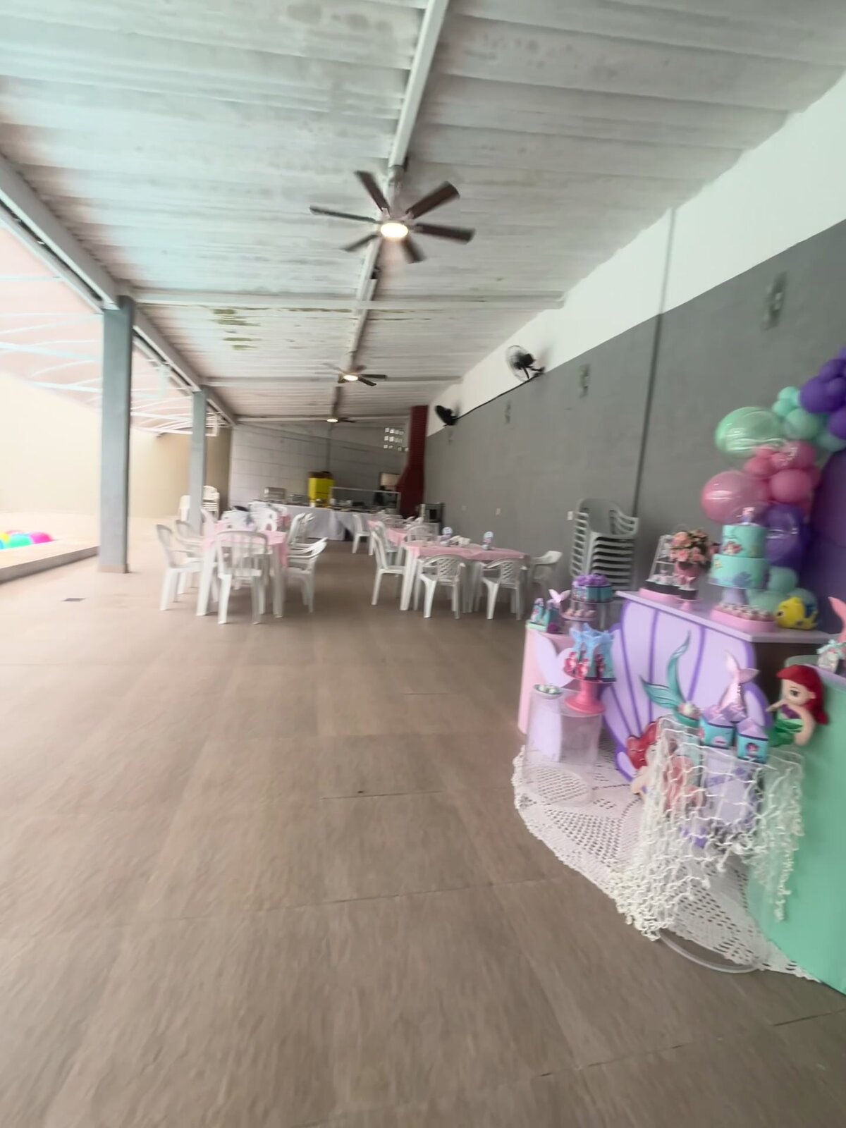 A área coberta comprida da Casa 2 com mesas montadas e a decoração de festa ao fundo.