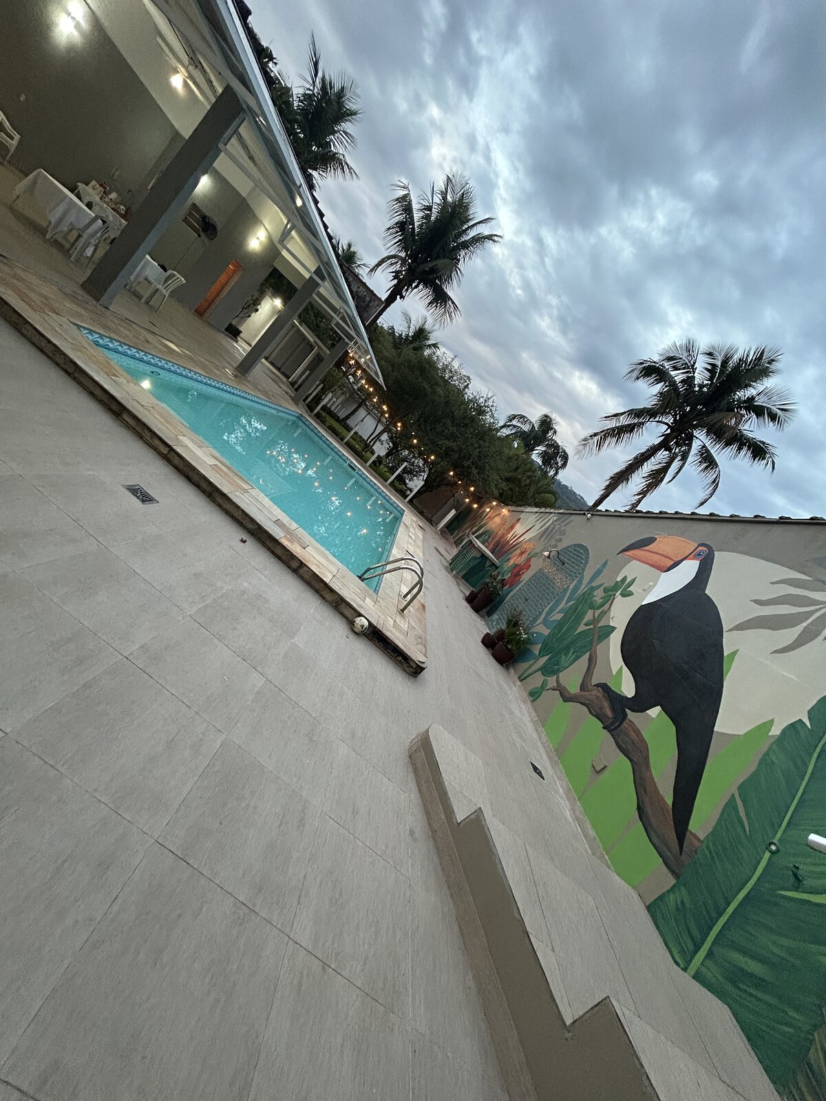Piscina da Casa 2 ao anoitecer, com os varais de luz acesos entre as palmeiras.