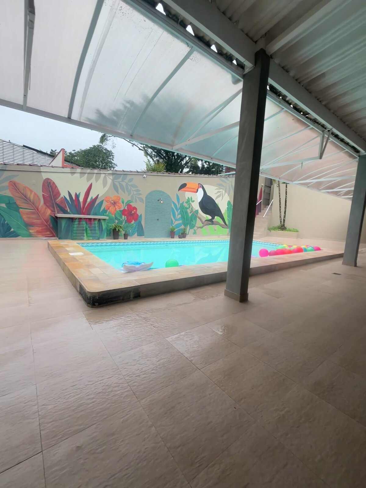 A piscina da Casa 2 vista de dentro da área coberta, com o mural ao fundo.