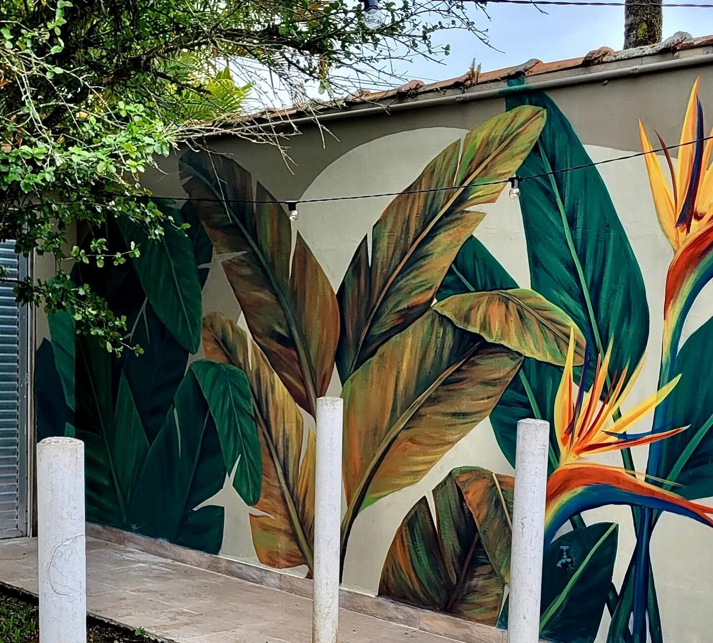 Estrelícias e folhas de bananeira pintadas no mural, entre as colunas da área coberta.